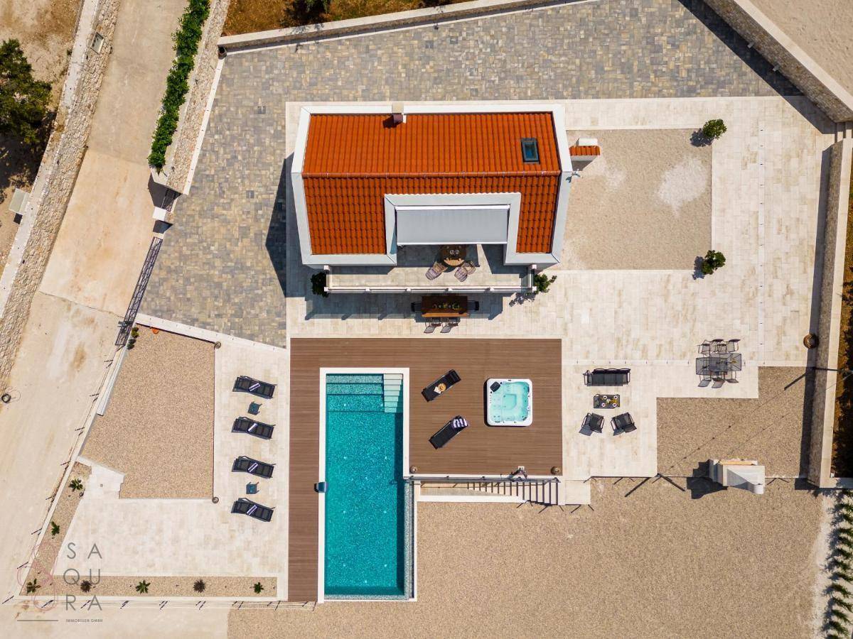 Vogelperspektive der modernen Villa mit Pool, Whirlpool und weitläufigen Außenbereichen unter blauem Himmel.