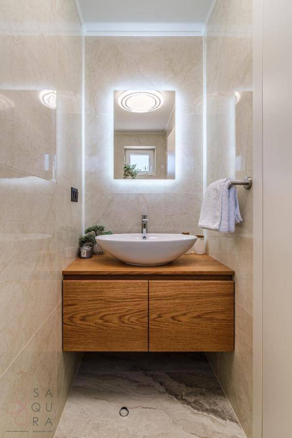 Kompaktes WC mit modernem Waschtisch, Holzunterschrank und beleuchtetem Spiegel.