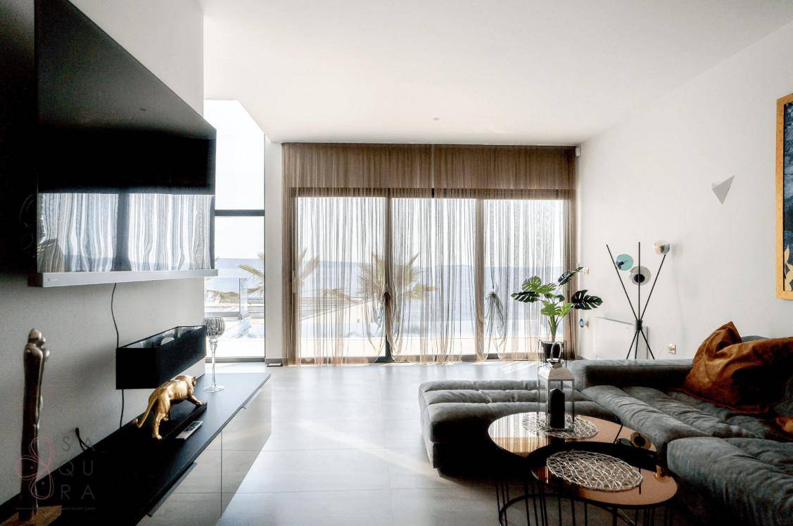 Helles Wohnzimmer mit großem Sofa, modernen Möbeln und bodentiefen Fenstern zum Meer.