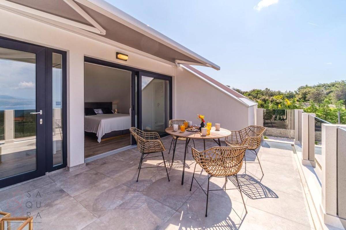 Sonnige Terrasse mit Esstisch und Stühlen, bietet einen schönen Blick auf das Meer.