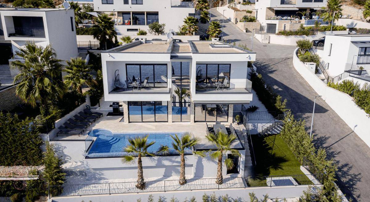 Luftaufnahme einer modernen Villa mit Poolbereich und umliegenden Häusern.
