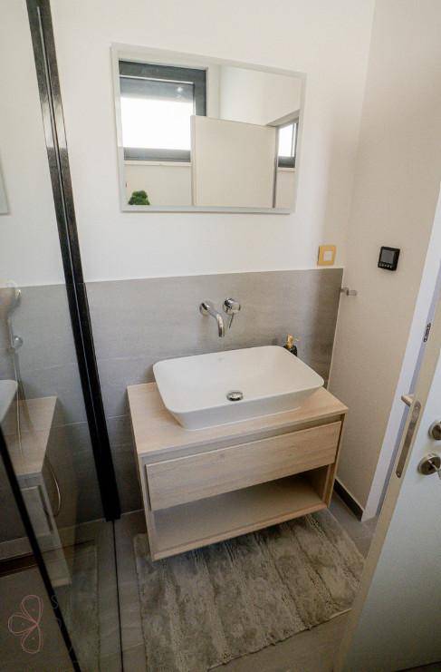 Modernes Badezimmer mit Einzelwaschbecken auf Holzunterschrank und großem Spiegel.