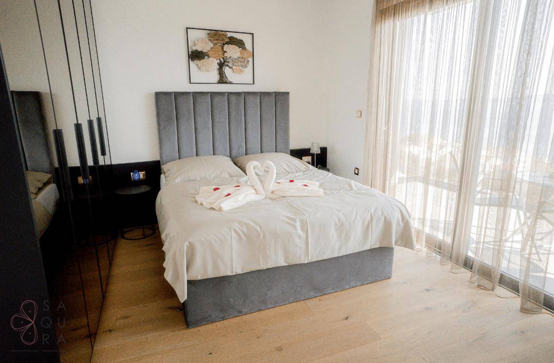 Helles Schlafzimmer mit großem Bett, gepolstertem Kopfteil und bodentiefen Fenstern.