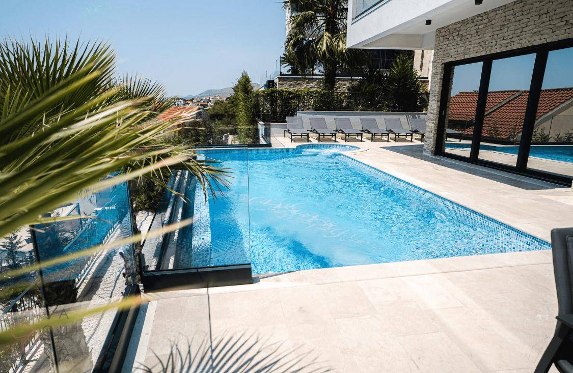 Großer Pool mit blauen Fliesen und Sonnenliegen, umgeben von einer hellen Terrasse.
