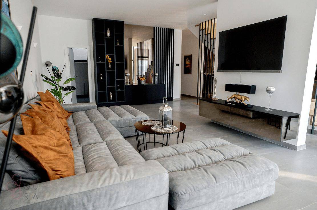 Geräumiges Wohnzimmer mit L-förmigem Sofa, Wandfernseher und offener Gestaltung.