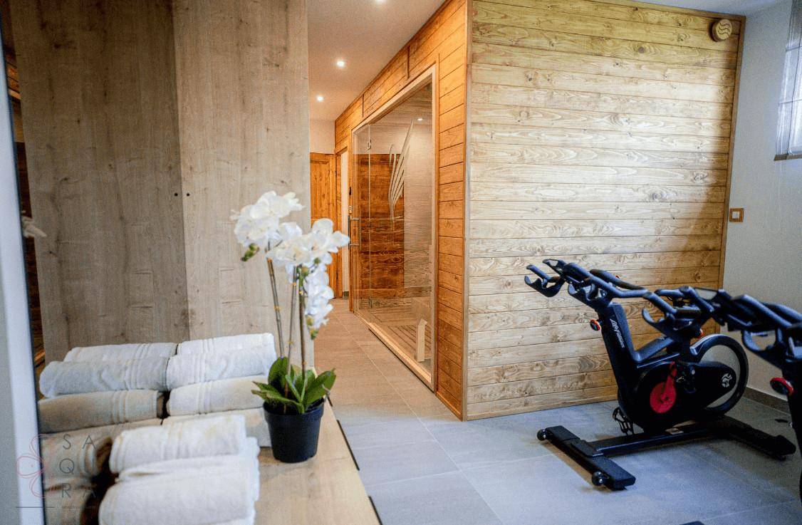 Wellnessbereich mit Fitnessgeräten und einer sichtbaren Sauna, umgeben von Holzvertäfelung.
