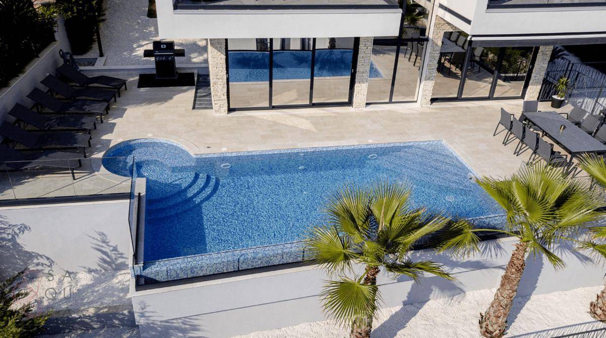 Detailansicht des Pools mit blauen Fliesen, Sonnenliegen und Essbereich im Freien.
