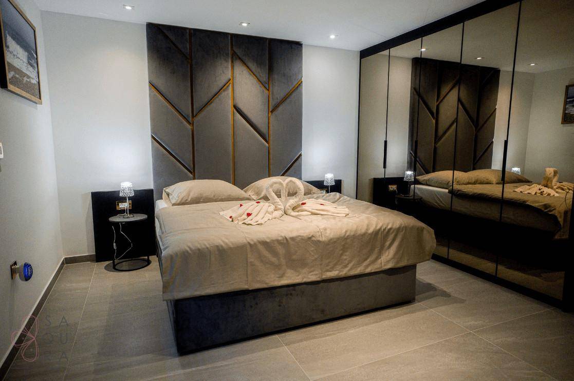 Elegantes Schlafzimmer mit großem Bett, gepolstertem Kopfteil und einer modernen Spiegelwand.