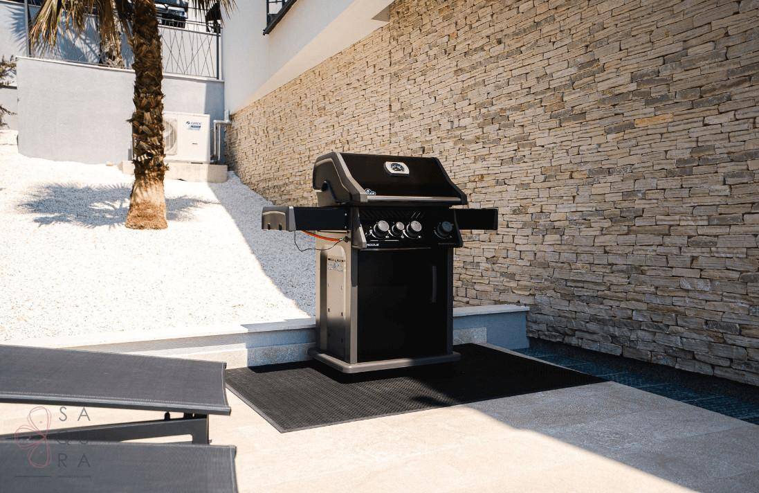 Außenbereich mit modernem Grill auf einer gepflasterten Terrasse und einer Steinwand.
