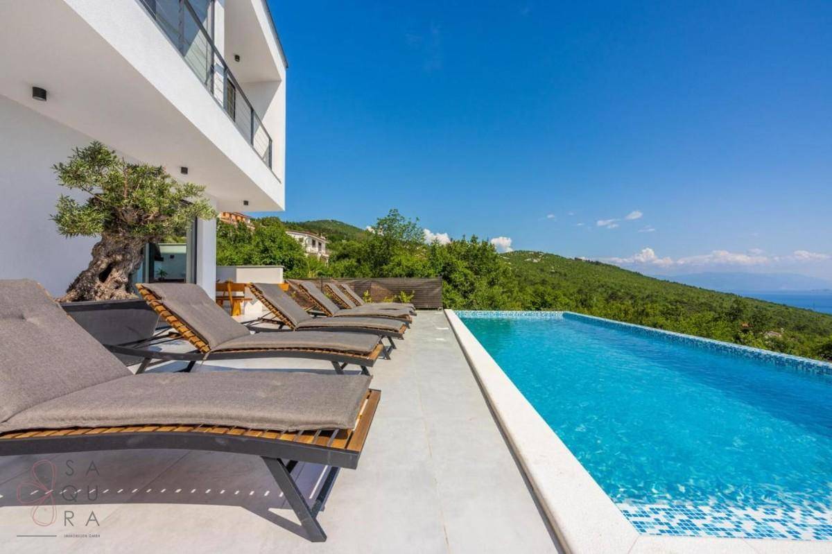 Entspannender Poolbereich mit Sonnenliegen und weitem Blick über die grüne Landschaft zum Meer.