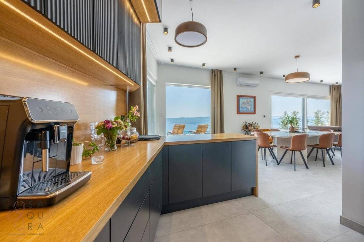 Moderne Küche mit Holzarbeitsplatte, Kaffeemaschine und offenem Blick auf den Essbereich und das Meer.