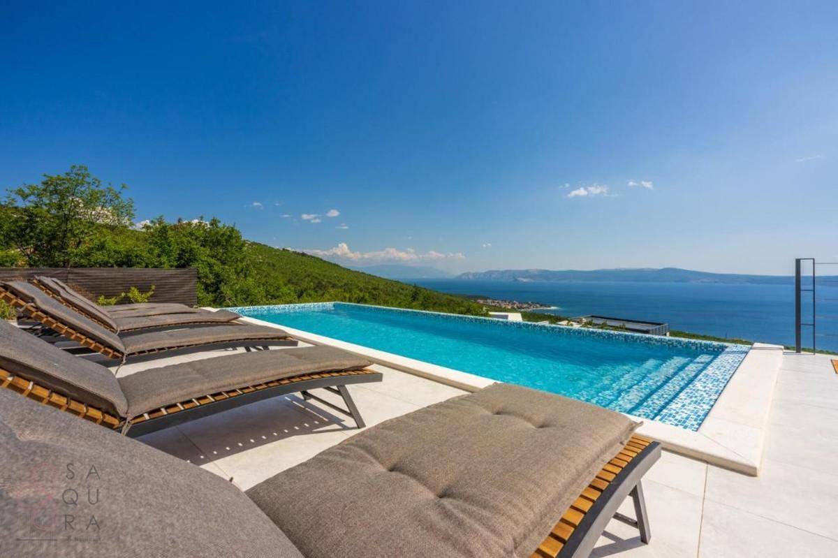 Entspannender Poolbereich mit Sonnenliegen und weitem Blick über die grüne Landschaft zum Meer.