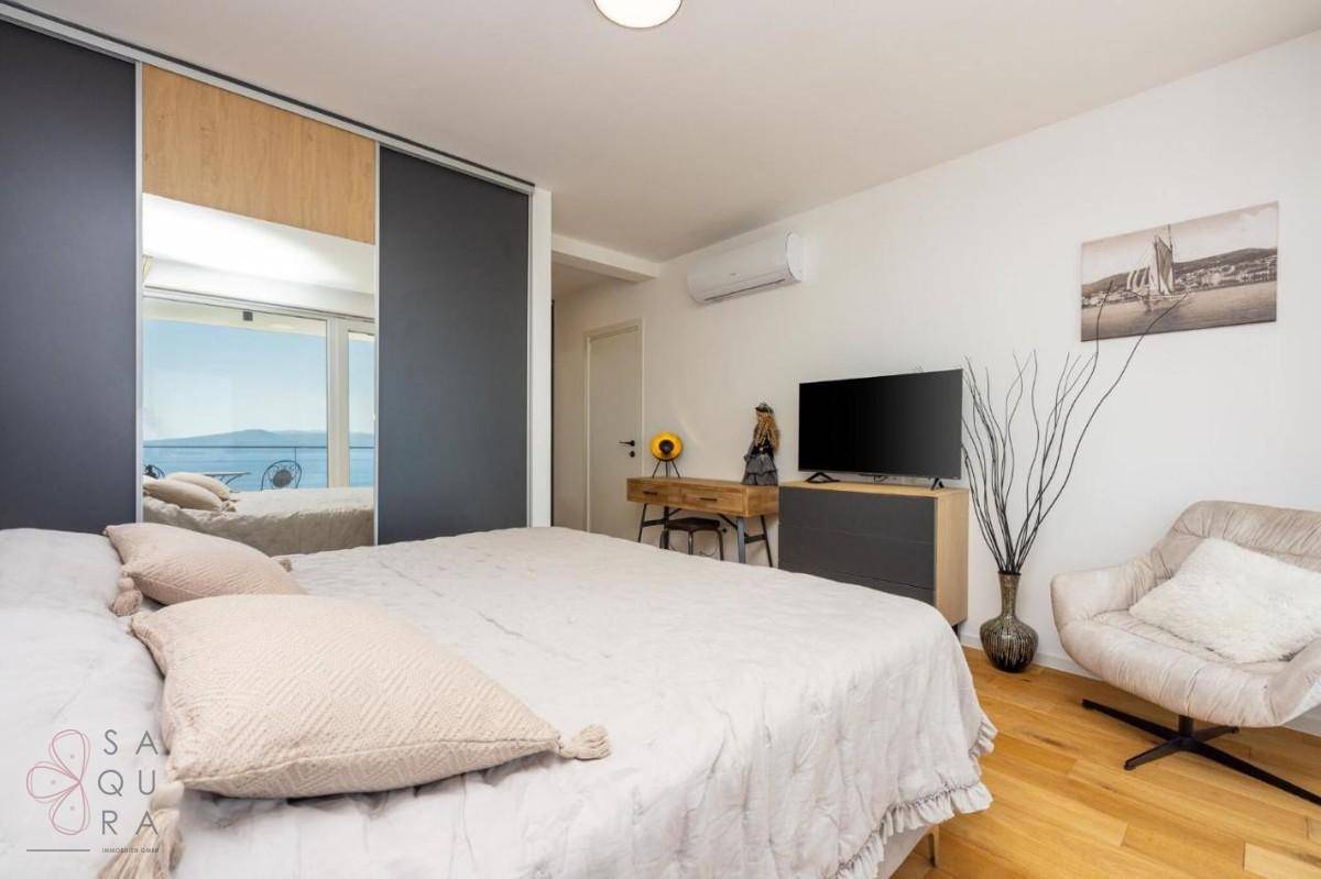 Helles Schlafzimmer mit großem Bett, Fernseher und Einbauschränken, die den Meerblick reflektieren.