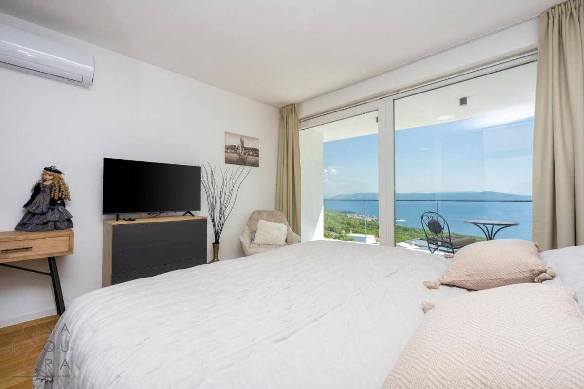 Helles Schlafzimmer mit großem Bett, Fernseher und raumhohen Fenstern mit atemberaubendem Meerblick.