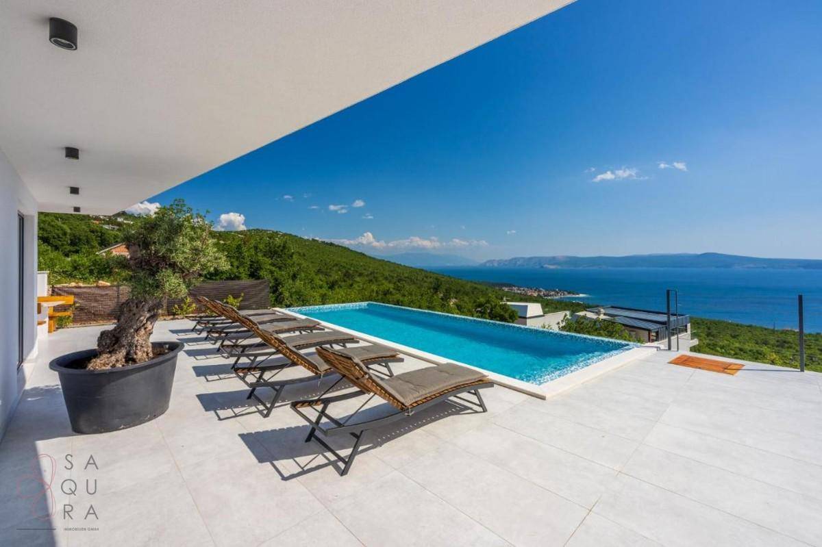 Entspannender Poolbereich mit Sonnenliegen und weitem Blick über die grüne Landschaft zum Meer.