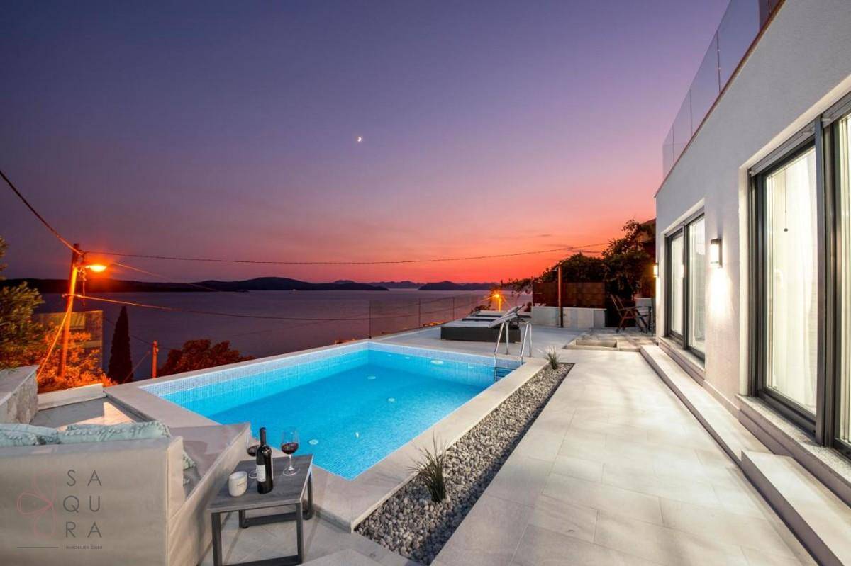 Beleuchteter Pool und Terrasse mit Lounge-Möbeln bei Sonnenuntergang, bieten einen malerischen Meerblick.