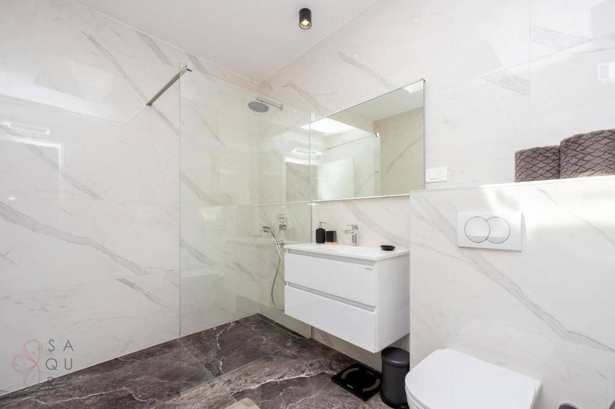 Modernes Badezimmer mit großer begehbarer Dusche, schwebendem Waschtisch und eleganten Marmorfliesen.