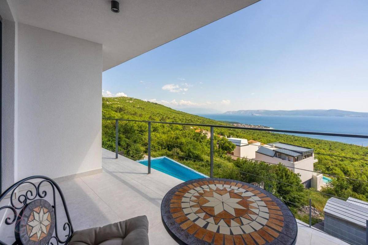 Sonniger Balkon mit Mosaiktisch und Stühlen, bietet einen weiten Blick auf das Meer und die Umgebung.