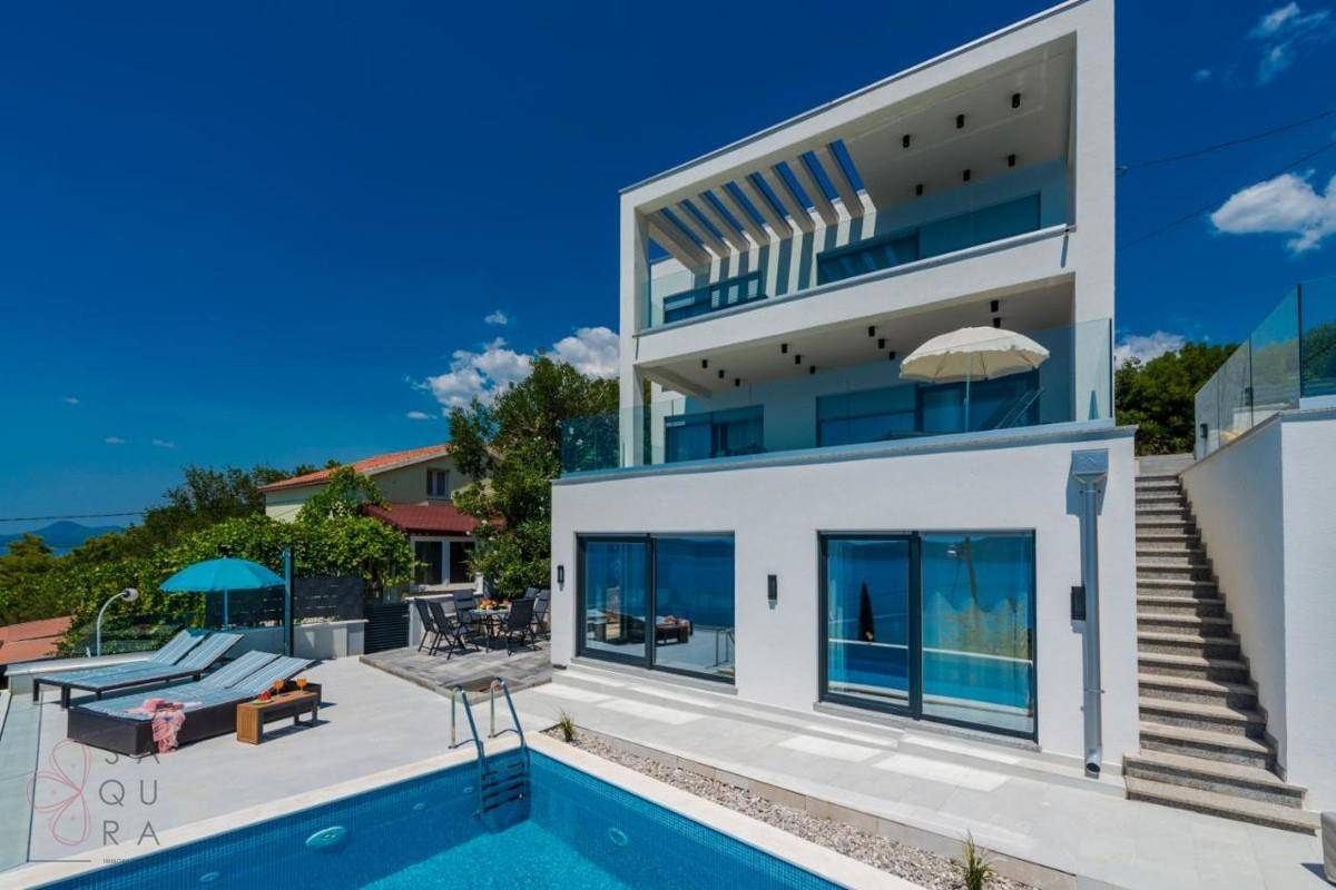 Elegante Villa mit privatem Poolbereich, Sonnenliegen und Meerblick unter strahlend blauem Himmel.