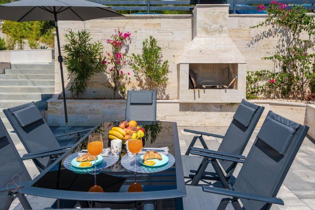 Detailaufnahme des Essbereichs im Freien mit Grillkamin und mediterranen Pflanzen.
