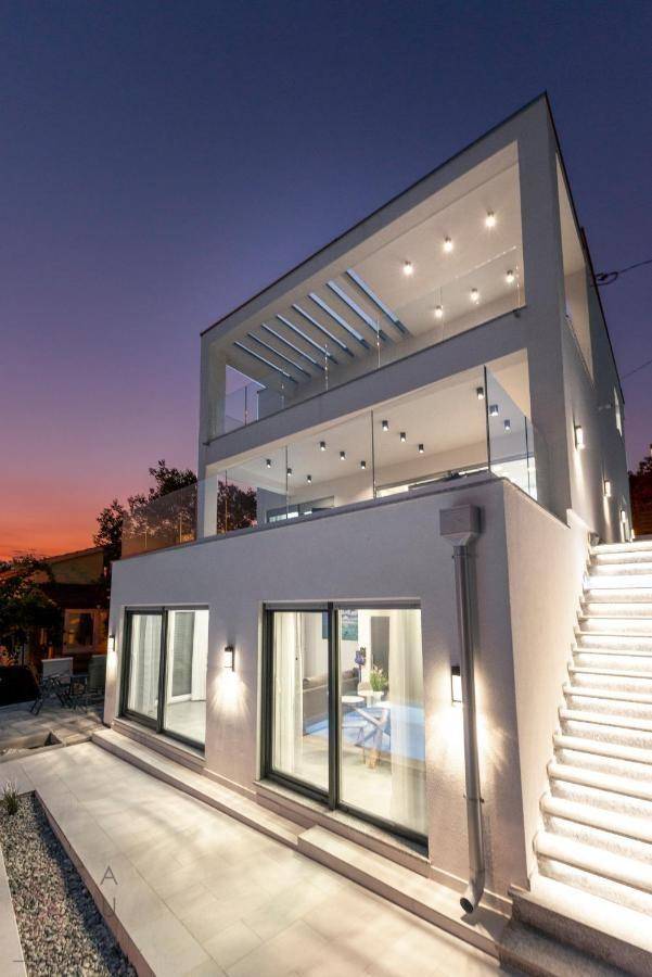 Moderne Villa bei Sonnenuntergang mit beleuchteten Terrassen und Außentreppe.