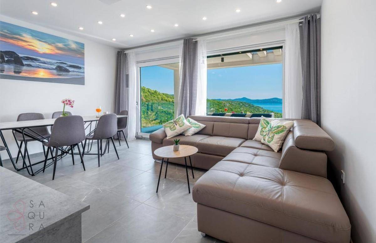 Offener Wohn-Essbereich mit modernem Sofa, Esstisch und weitem Meerblick durch große Fenster.