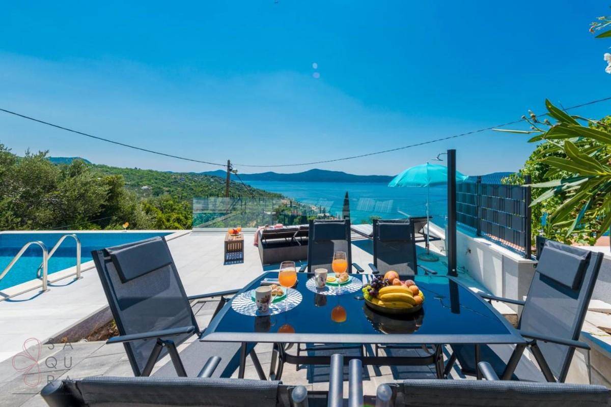 Essbereich im Freien neben dem Pool mit Blick auf das glitzernde Meer und die Küste.