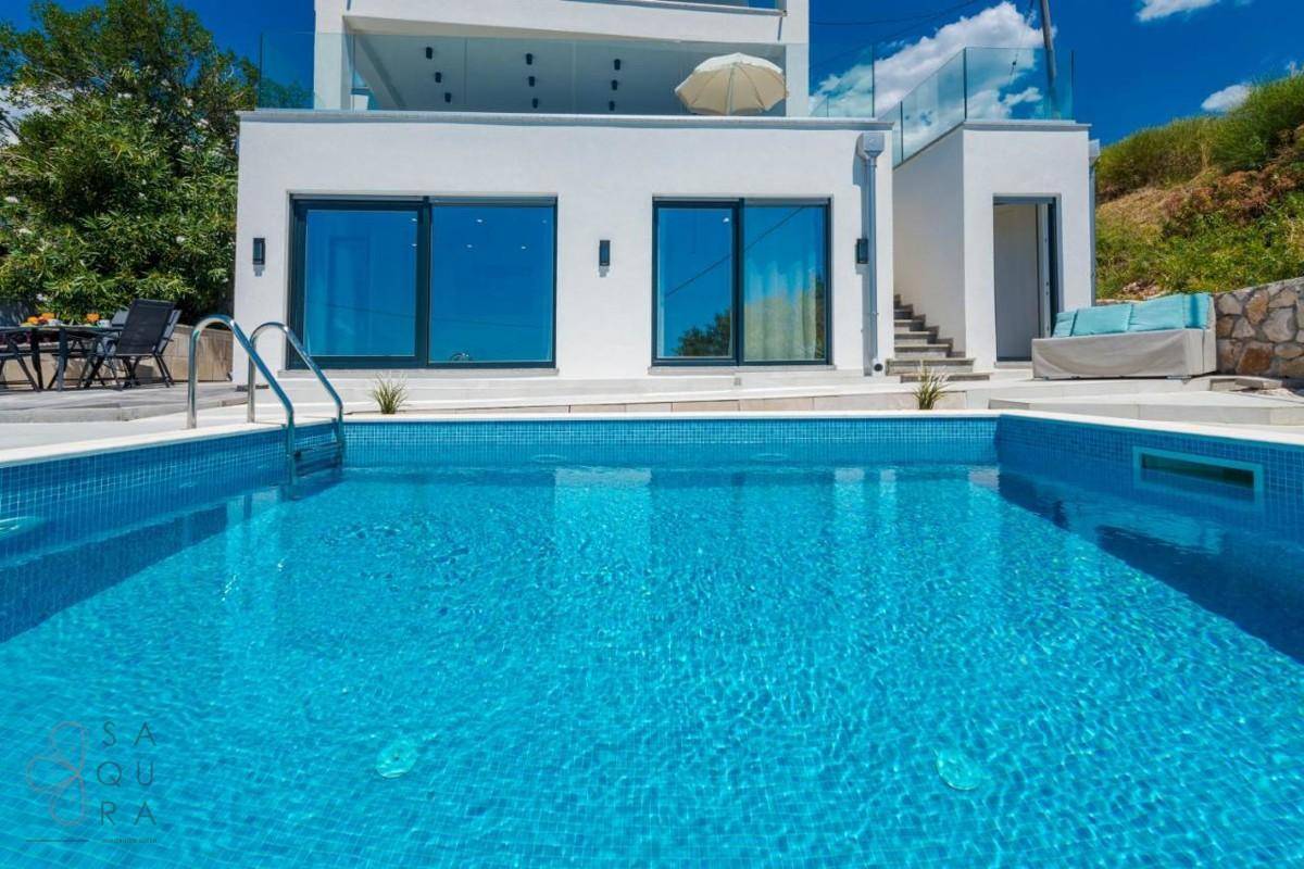 Blauer Mosaikpool vor der modernen Villa mit großen Fenstern und klarem Himmel.