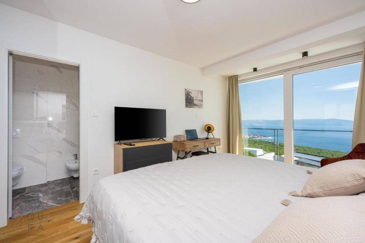 Helles Schlafzimmer mit großem Bett, Fernseher und Zugang zu einem modernen Bad, mit Meerblick.