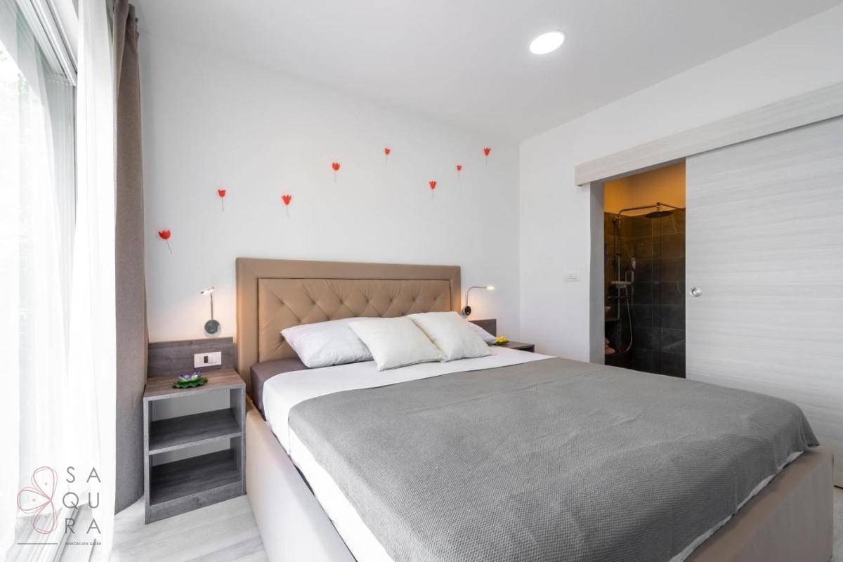 Modernes Schlafzimmer mit hellem Laminatboden und direktem Zugang zum Badezimmer.