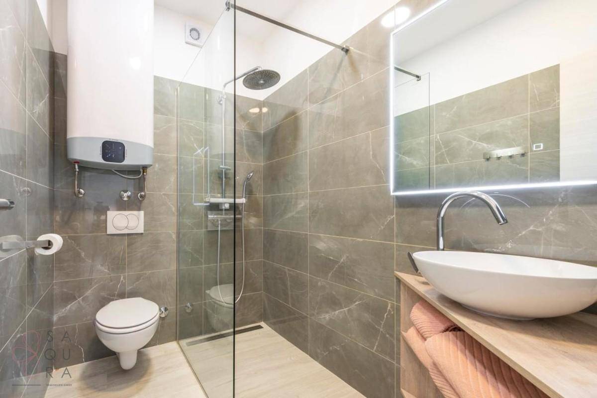 Modernes Badezimmer mit begehbarer Dusche, Wand-WC und eleganten grauen Fliesen.
