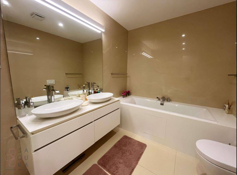 Modernes Badezimmer mit Doppelwaschbecken, Badewanne und großen beigen Fliesen, strahlt Eleganz aus.