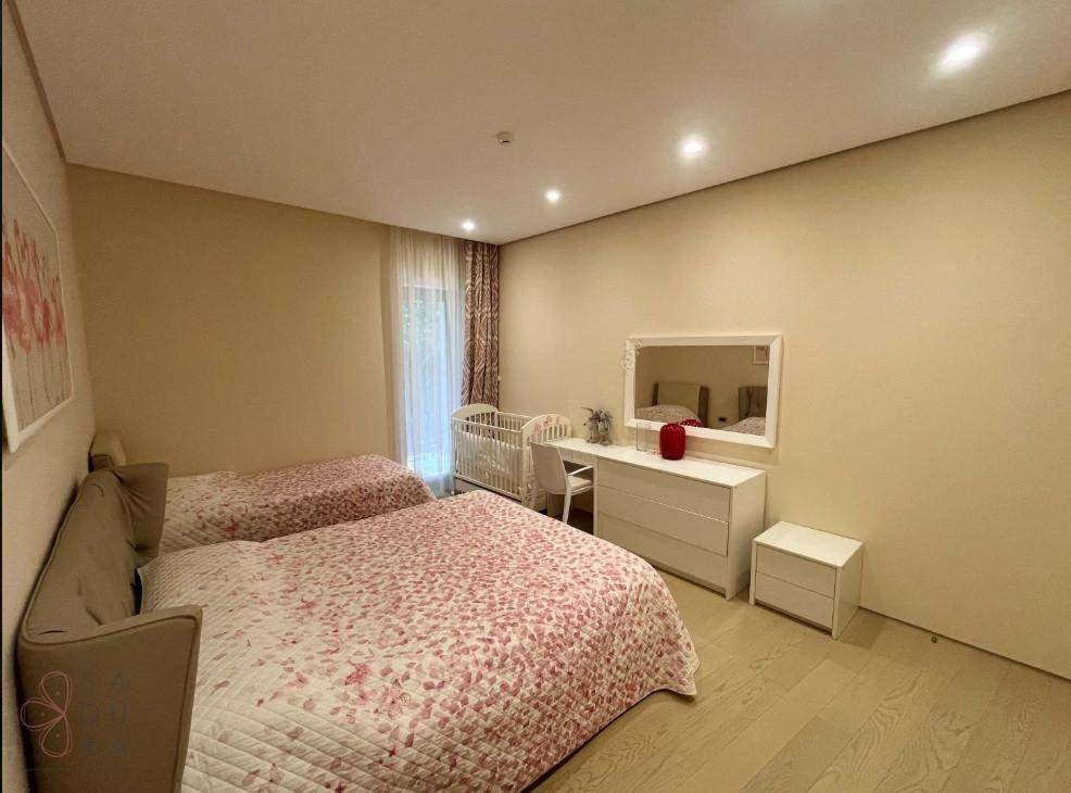 Helles Schlafzimmer mit zwei Einzelbetten, Babybett und Kommode mit Spiegel.