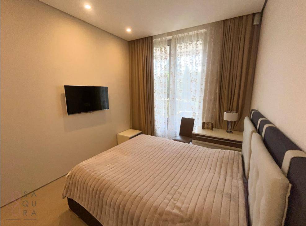 Gemütliches Schlafzimmer mit Doppelbett, Wandfernseher und Vorhängen, bietet eine ruhige grüne Aussicht.