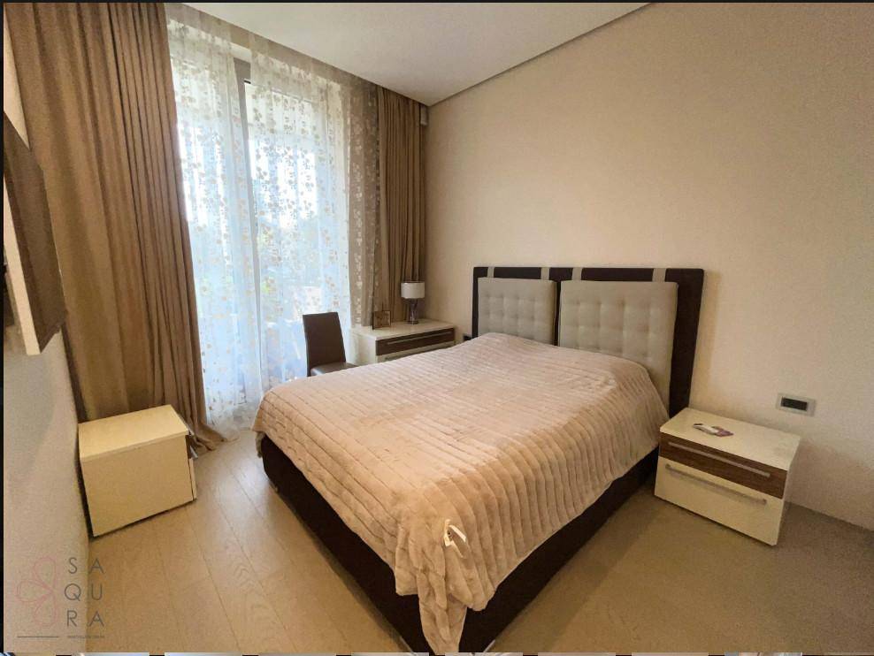 Helles Schlafzimmer mit großem Fenster, beigem Teppich und modernen Nachttischen, bietet eine grüne Aussicht.