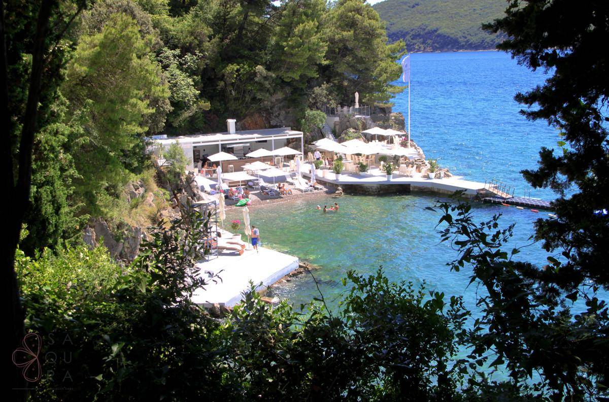 Malerische Bucht mit Restaurant, Strand und klarem Meerwasser, umgeben von üppiger Vegetation.