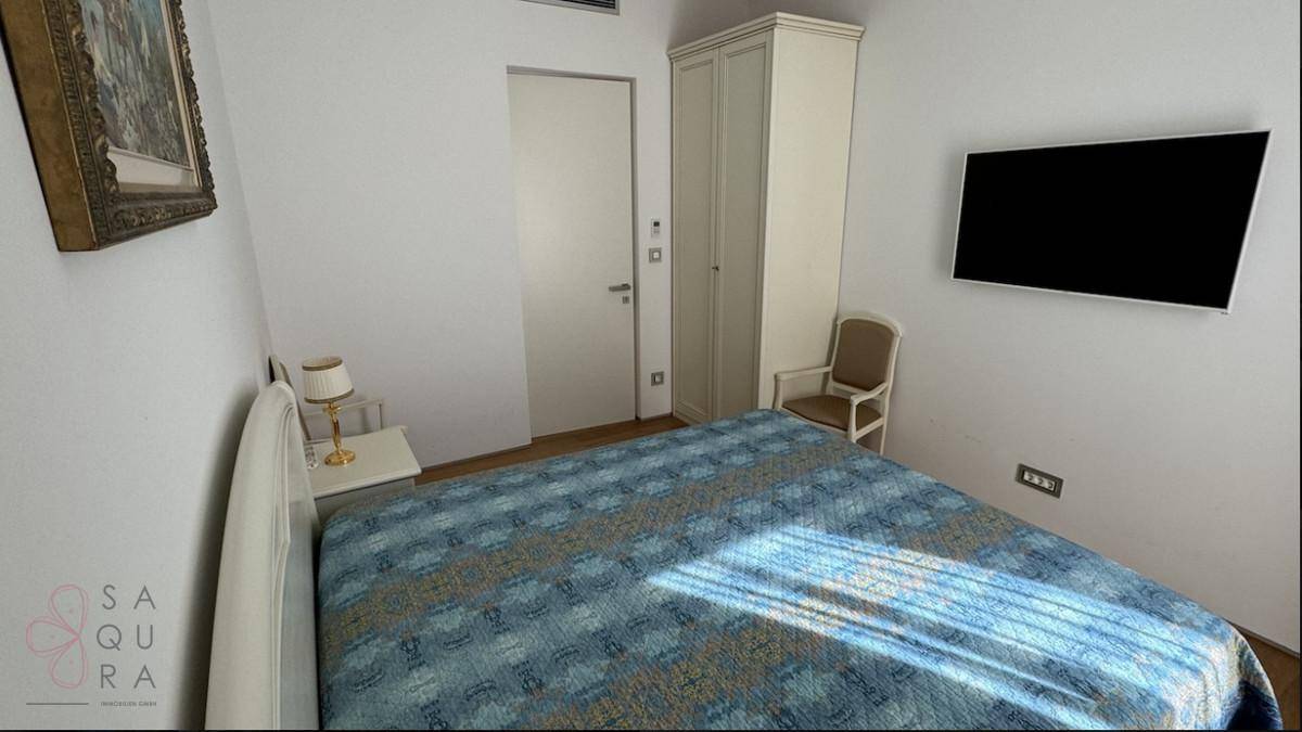 Schlafzimmer mit Doppelbett, Kleiderschrank und an der Wand montiertem Fernseher.