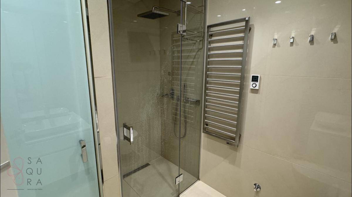 Detaillierte Ansicht der modernen begehbaren Dusche mit Regenduschkopf und Glasabtrennung im Badezimmer.