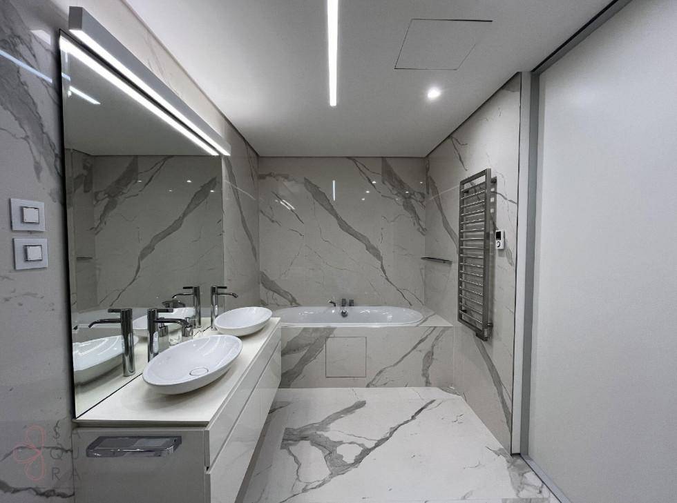 Luxuriöses Badezimmer mit Marmorfliesen, Doppelwaschbecken und integrierter Badewanne, sehr stilvoll.