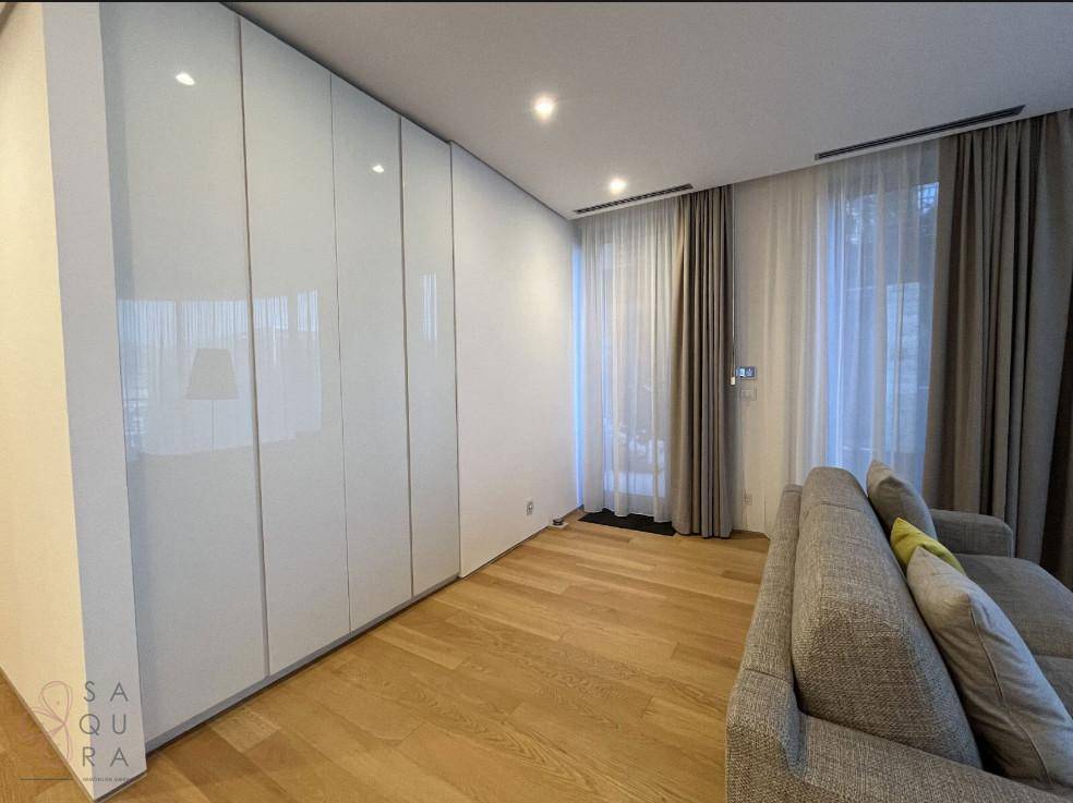 Helles Zimmer mit modernen Einbauschränken, Holzfußboden und großen Fenstern mit Vorhängen.