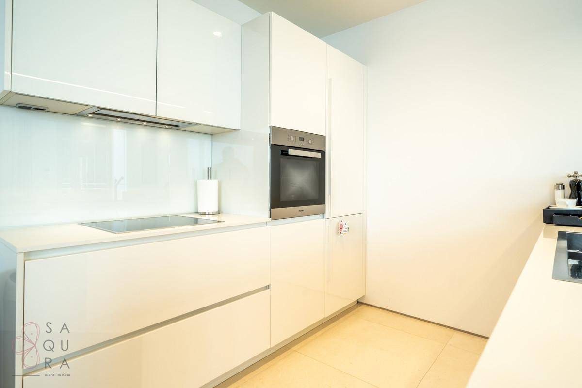 Moderne, helle Küche mit weißen Hochglanzfronten, integriertem Backofen und Induktionskochfeld.