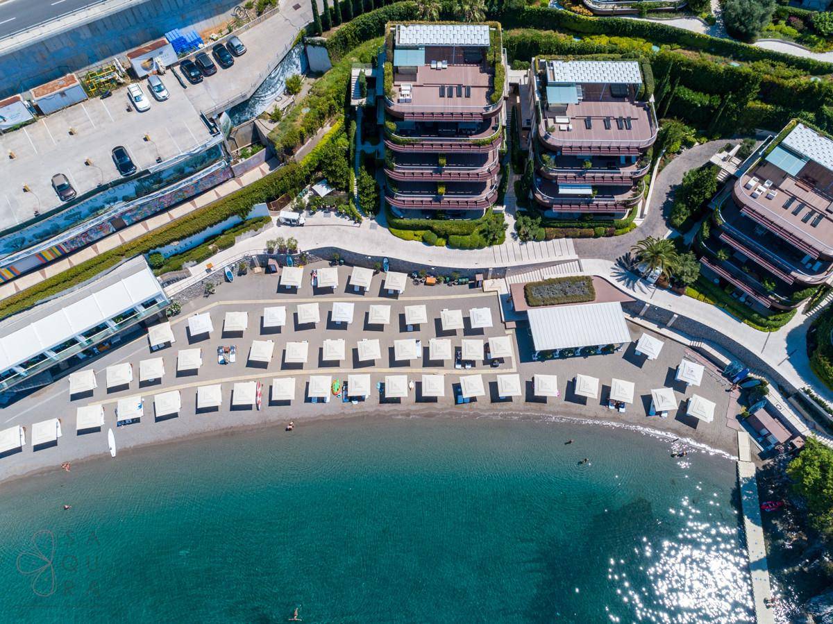 Luftaufnahme einer luxuriösen Wohnanlage mit Privatstrand, Sonnenschirmen und klarem Meerwasser.