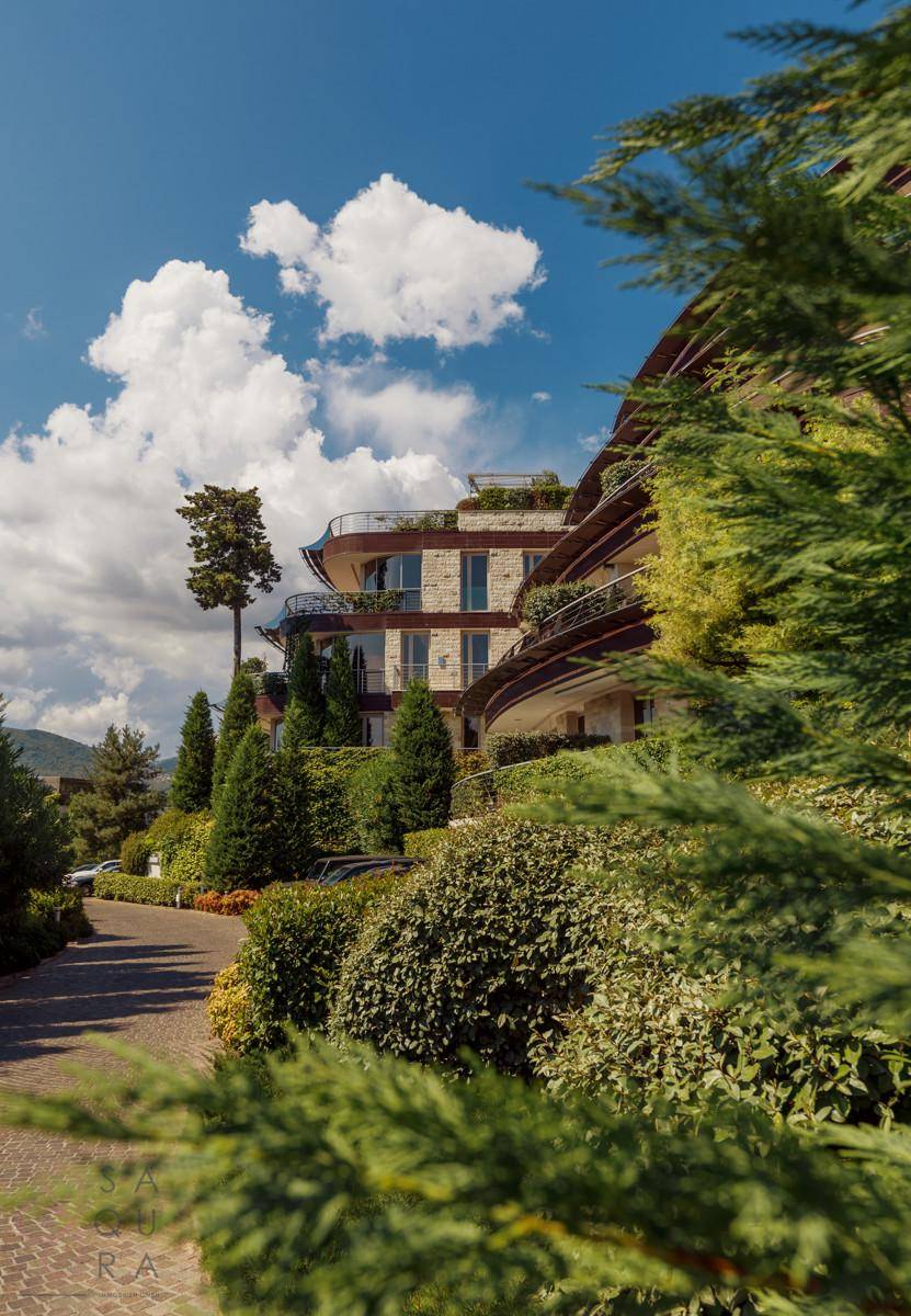 Elegantes Gebäude mit geschwungenen Balkonen, eingebettet in eine gepflegte Gartenanlage mit Zufahrtsweg.