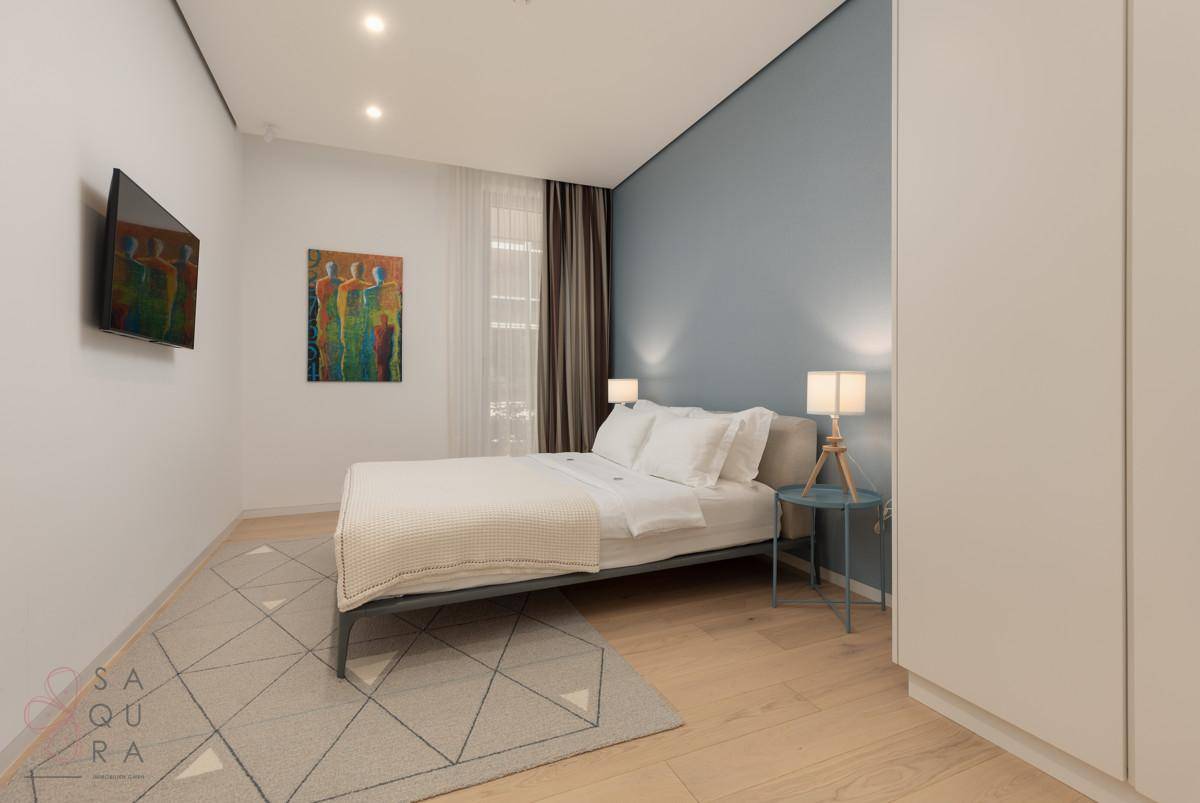 Ein stilvolles Schlafzimmer mit Doppelbett, blauer Akzentwand und einem modernen Teppich auf Holzfußboden.
