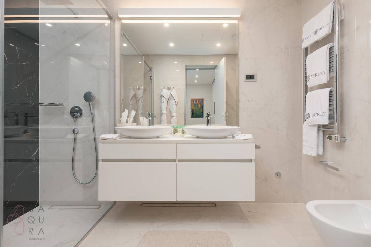 Modernes Badezimmer mit Doppelwaschbecken, großer Dusche und eleganten Marmorfliesen.