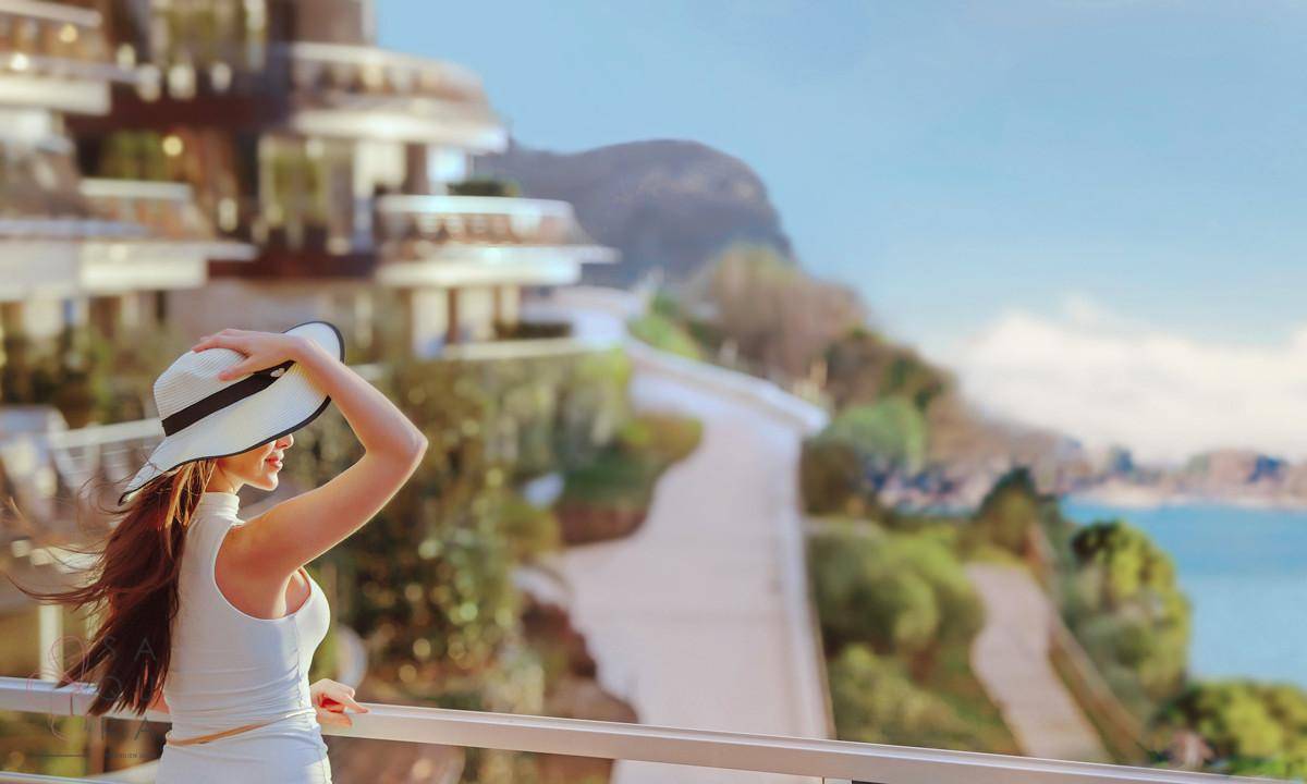 Eine Frau steht auf einem Balkon und genießt den weiten Blick auf das Meer und die Küstenlandschaft.