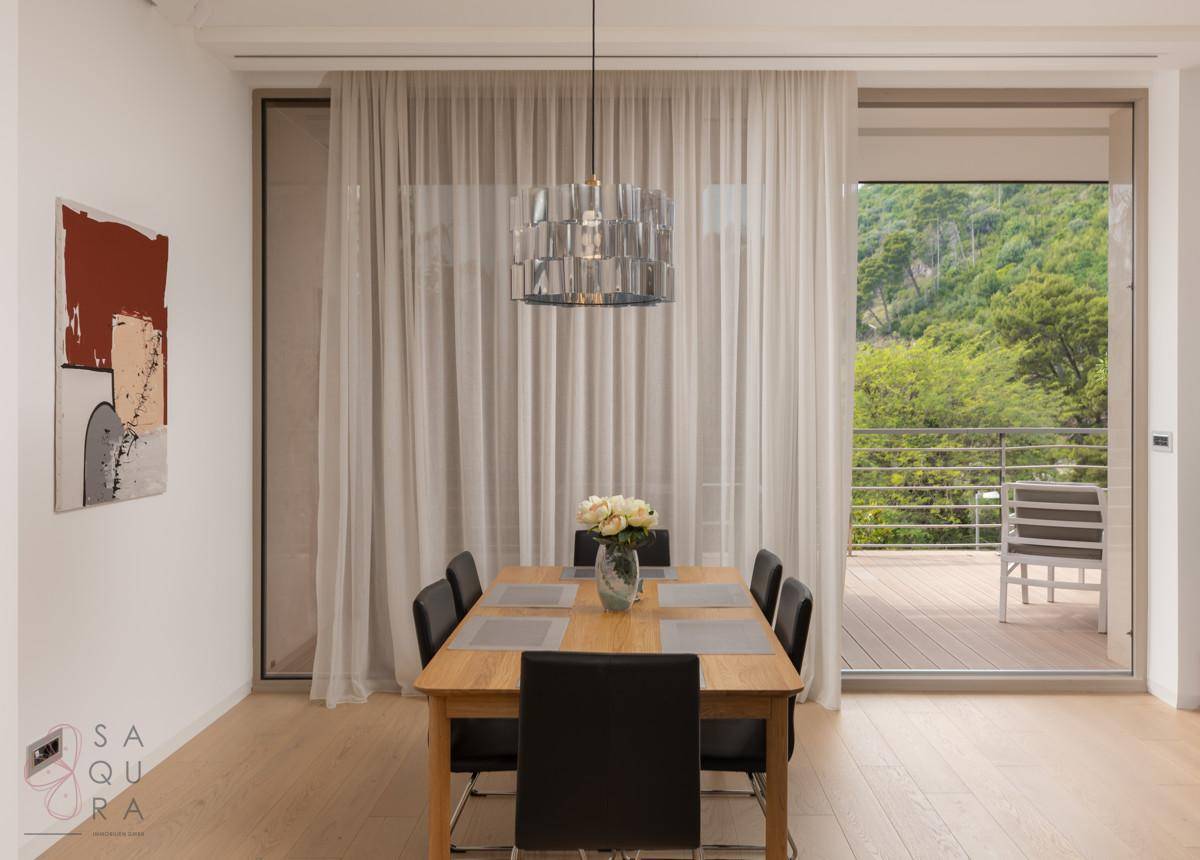 Ein heller Essbereich mit Holztisch und schwarzen Stühlen, mit Zugang zu einem Balkon und Blick ins Grüne.