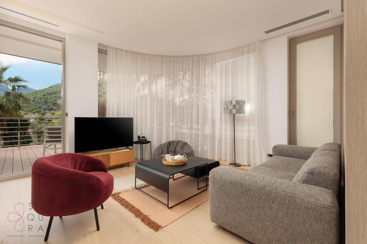 Ein modernes Wohnzimmer mit bequemen Sofas, einem Fernseher und Zugang zu einem Balkon mit Bergblick.