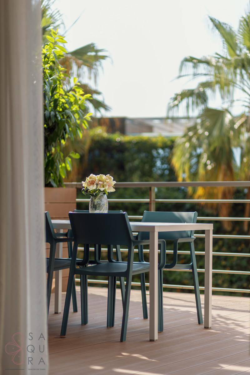Sonniger Balkon mit Essbereich und Blick auf die umliegenden Palmen und Grünflächen.