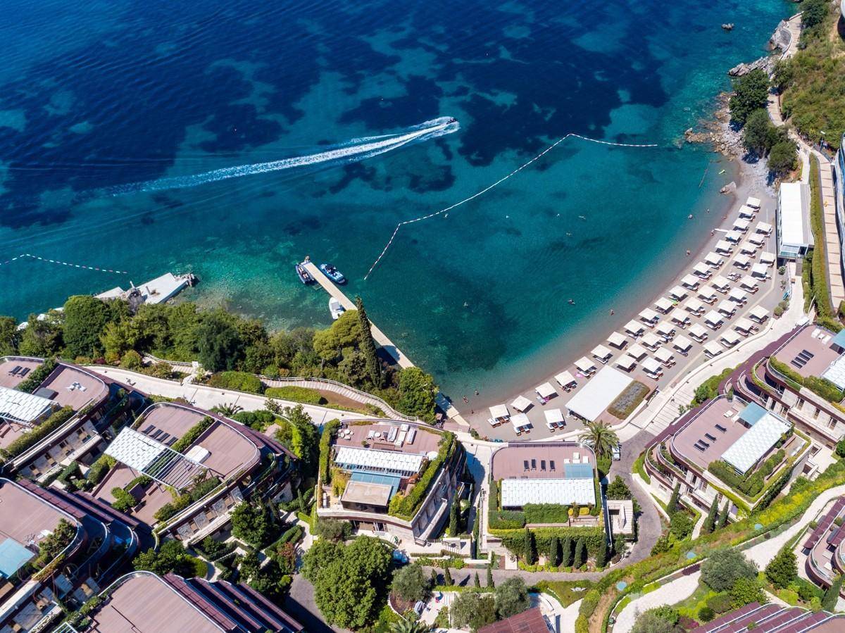 Luftaufnahme einer luxuriösen Küstenanlage mit Villen, Strand und klarem türkisfarbenem Wasser.